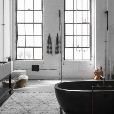 Elegant double vanity bathroom with grey cabinetry, marble countertops, and large mirrors. The room features modern lighting and a central bench.